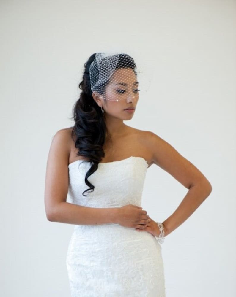 May include: A bride wearing a white strapless wedding dress with a veil and a delicate bracelet. Her hair is styled in a long, flowing ponytail.