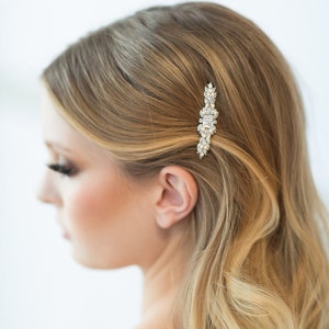 May include: A silver hair comb with clear crystal embellishments. The comb is designed with a cluster of crystals in the centre and smaller crystals extending out on either side.