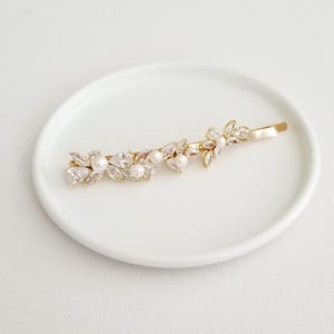 May include: Gold-toned hair barrette featuring a floral design with clear crystals and faux pearls. The barrette is approximately 3 inches long and is designed to add a touch of elegance to any hairstyle.