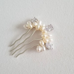 Puede incluir: Un peine de pelo plateado con un grupo de perlas blancas y brillantes transparentes. El peine tiene una forma curva y est&aacute; dise&ntilde;ado para agregar un toque de elegancia a los peinados.