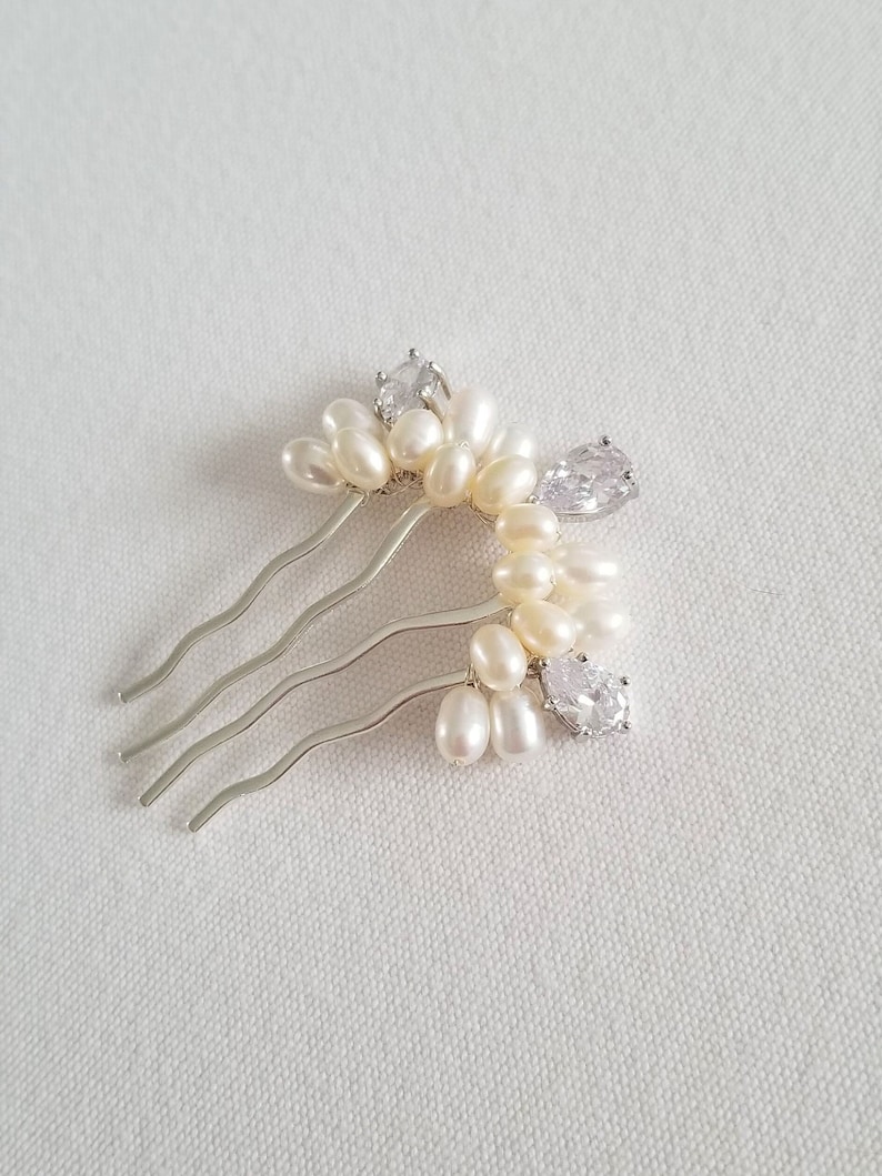 Puede incluir: Un peine de pelo plateado con un grupo de perlas blancas y brillantes transparentes. El peine tiene una forma curva y est&aacute; dise&ntilde;ado para agregar un toque de elegancia a los peinados.