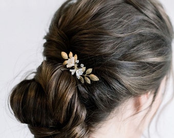 May include: A gold hair comb with white flowers and leaves. The comb is in a woman's hair.
