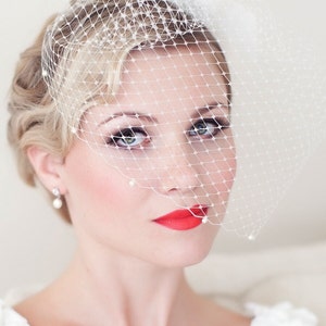 May include: A bride with blonde hair wearing a white veil with pearl accents and a red lipstick.