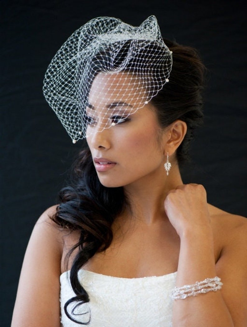 May include: A bride wearing a white wedding dress with a white veil and pearl earrings. Her hair is styled in a side part with loose curls.