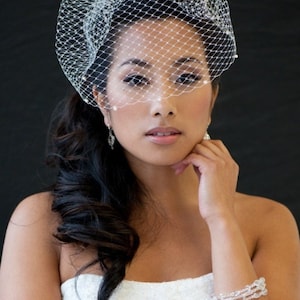 May include: A bride with long dark hair wears a white strapless gown and a white veil with pearl accents. She is wearing a crystal bracelet on her wrist.