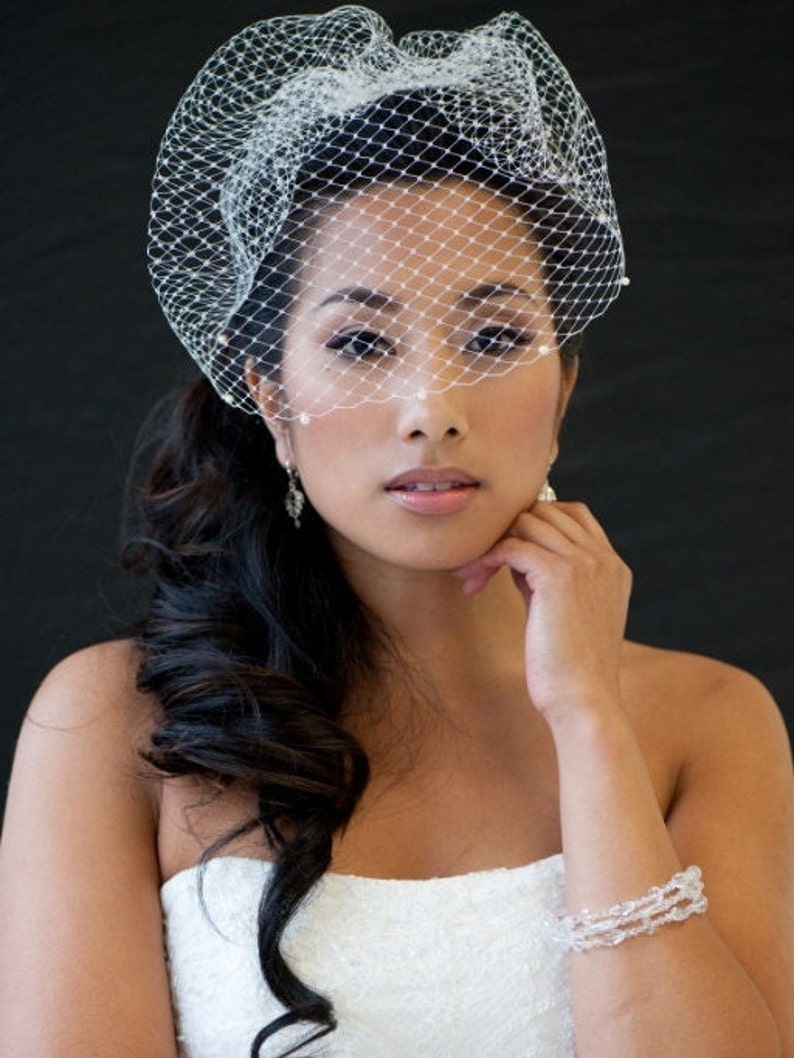May include: A bride with long dark hair wears a white strapless gown and a white veil with pearl accents. She is wearing a crystal bracelet on her wrist.