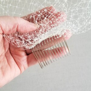 May include: A white bridal veil with a silver comb attached to the bottom edge. The comb has a row of teeth that are designed to hold the veil in place in the hair.