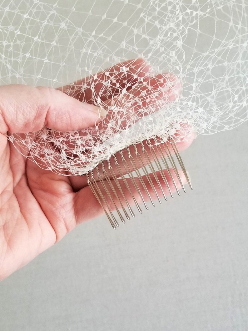 May include: A white bridal veil with a silver comb attached to the bottom edge. The comb has a row of teeth that are designed to hold the veil in place in the hair.