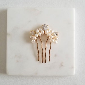 Puede incluir: Peine de pelo dorado con detalles de perlas blancas y diamantes de imitaci&oacute;n transparentes. El peine tiene una forma curva y cuatro p&uacute;as.