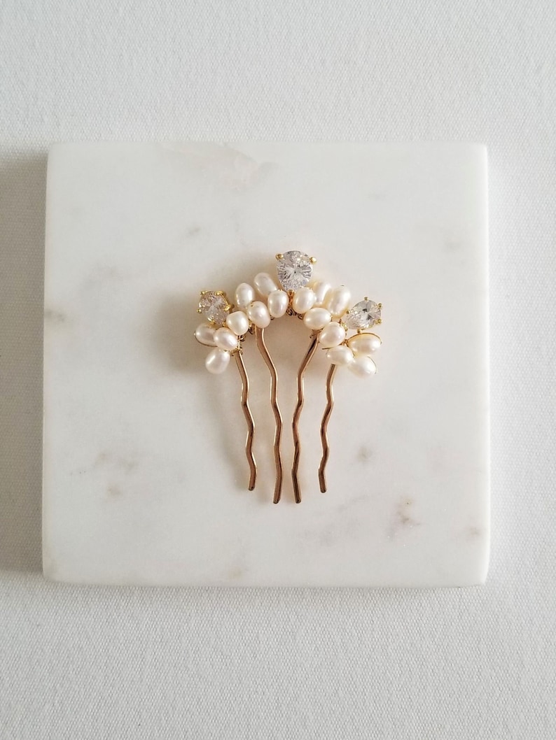 Puede incluir: Peine de pelo dorado con detalles de perlas blancas y diamantes de imitaci&oacute;n transparentes. El peine tiene una forma curva y cuatro p&uacute;as.
