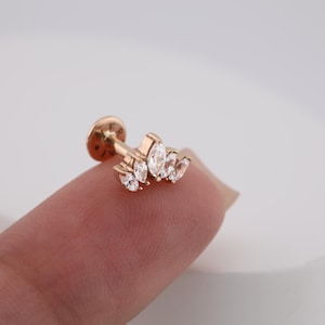 Puede incluir: Un pendiente de piercing para el labio de oro rosa con un grupo de piedras de circonita cúbica transparentes con corte marquesa. El pendiente tiene una parte trasera plana y un pequeño disco redondo. Para piercing corporal.