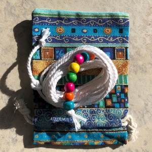 May include: A white drawstring bag with a colourful beaded necklace inside. The bag has a blue, gold and orange patterned design.
