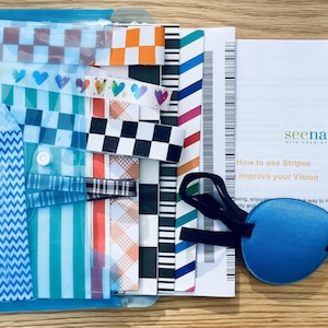 May include: A collection of vision therapy tools, including striped and patterned overlays, a blue eye patch, and a pamphlet with the text "seenaturally". The overlays feature various designs, such as hearts, stripes, and checkered patterns.