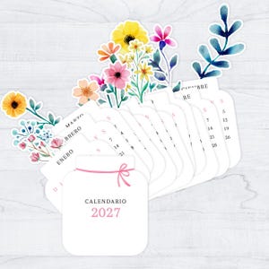 May include: A 2027 calendar set featuring white cards shaped like mason jars with pink string illustrations. Each card displays a month name in Spanish, such as Enero, Febrero, and Marzo, alongside watercolor floral accents in yellow, pink, and blue.