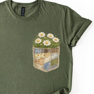 Könnte beinhalten: Olivgrünes T-Shirt mit einem Taschen-Design mit einem Patchwork aus Gänseblümchen. Die Tasche besteht aus Patchwork-Stoff in verschiedenen Mustern und Farben, darunter Blau, Gelb und Braun. In der Mitte der Tasche befindet sich ein brauner Knopf.