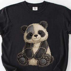 May include: Black t-shirt with a panda bear illustration. The panda has a patchwork design with black and cream-coloured sections, stitched together with visible thread. The panda's face has black eyes and a small smile.