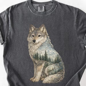 May include: Dark gray t-shirt featuring a seated wolf illustration. The wolf's body incorporates a landscape of trees and mountains. The shirt has rolled-up sleeves and a crew neck.