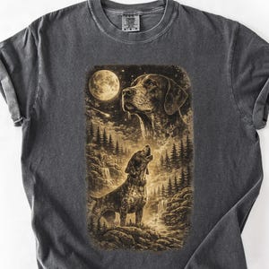 Pode incluir: Camiseta cinza escuro com um gráfico em tons de sépia de um cão uivando para a lua. O design inclui uma floresta, uma cachoeira e a cabeça de um segundo cão. A camiseta tem gola redonda e mangas curtas.