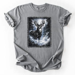 K&ouml;nnte beinhalten: Graues T-Shirt mit einer Schwarz-Wei&szlig;-Illustration eines Hirsches in einem Wald. Der Hirsch hat ein gro&szlig;es Geweih und steht in einer nebligen Gegend. Das T-Shirt hat einen Rundhalsausschnitt und kurze &Auml;rmel.