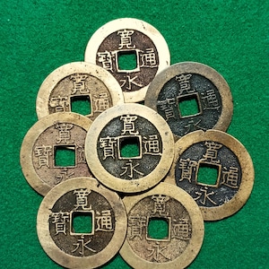 Peut inclure: Huit pièces de monnaie chinoises anciennes avec un trou carré au centre et des caractères chinois sur le devant. Les pièces sont en laiton et ont un aspect usé et vieilli.