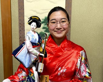 Beautiful and cute geisha doll. Holding aJapanese guitarinher hand, she is dressed in a luxurious light blue and blue costume. Height: 45 cm