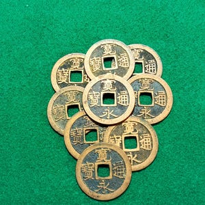 以下が含まれることがあります： 中央に正方形の穴が開いた中国の硬貨が10枚あります。硬貨はブロンズ製で、中国語の文字が刻まれています。硬貨は緑色のフェルトの表面に円形に並べられています。