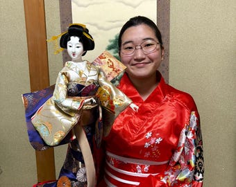 Cute and beautiful geisha doll. Holding a fan in herhand, she wears a luxurious costume with silver and blue flower patterns. Height: 55 cm.