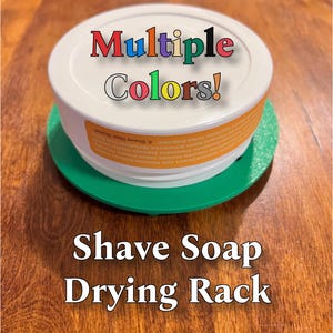 May include: A white shave soap drying rack with the words "Multiple Colors!" in rainbow colors on the top. The rack is made of plastic and has a green base. The text "Shave Soap Drying Rack" is written below the rack.