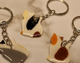 Può includere: Tre portachiavi a forma di gatto con anelli argentati. Ogni portachiavi presenta un motivo di colore diverso: grigio e bianco, tartarugato e arancione e marrone. I portachiavi sono realizzati in materiale lucido.