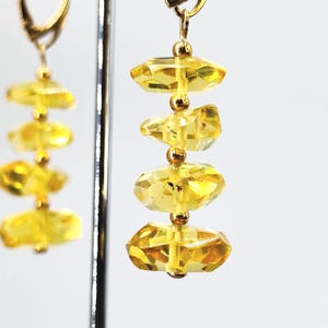 Könnte beinhalten: Ein Paar Ohrhänger mit facettierten, gelbgoldfarbenen Perlen. Jeder Ohrring hat einen goldfarbenen Haken und kleine goldene Perlen, die die größeren, geometrischen Perlen trennen. Die Ohrringe werden vor einem weißen Hintergrund präsentiert.