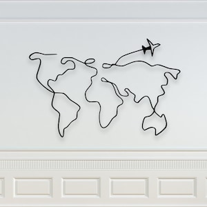 May include: Black metal wall art depicting a continuous line drawing of a world map with an airplane. The artwork is mounted on a white wall above a decorative panel.