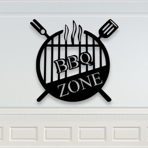 Könnte beinhalten: Schwarzes Metallschild mit der Aufschrift „BBQ ZONE“, Grillmotiv, Flammen und gekreuzten Grillutensilien. An einer weißen Wand mit Zierleisten befestigt.