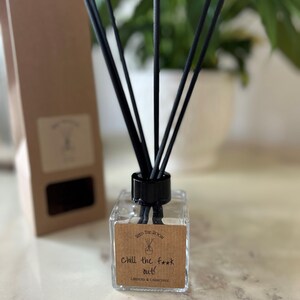 Op de afbeelding: Een diffuser van helder glas met zwarte rietjes en een bruin etiket met de tekst "Chill the f*** out!"  Lavendel & Kamille.