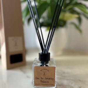 May include: A clear glass bottle with a black lid and black diffuser sticks. The bottle has a brown label that reads "Reed the Room Eau De Sweaty Bollocks  Rosemary, Orange & Fresh Coconut".