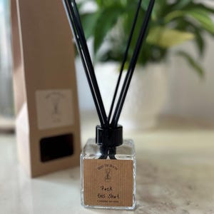 May include: A clear glass bottle diffuser with black reeds and a brown label that reads "Fill the Room" and "F*ck This Sh*t" with the text "Cassia and Musk" underneath.