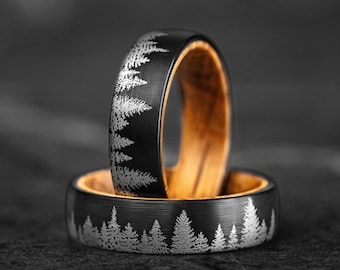 May include: Two black rings with a silver forest design. The rings have a wooden interior. The rings are set against a dark background. The rings are likely wedding bands or fashion accessories.
