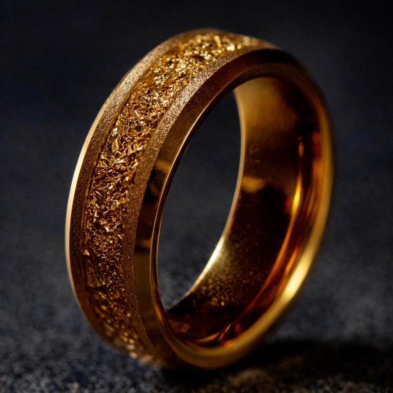 Op de afbeelding: Een goudkleurige ring met een getextureerde middenband. De ring heeft een gladde, gepolijste buitenrand en een ruwe, korrelige textuur in het midden. De ring is gemaakt van een glanzend, metalen materiaal.