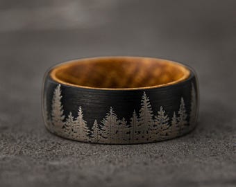 May include: A black tungsten carbide ring with a wood inlay and a silver etched design of a forest silhouette.