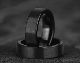 May include: Two black rings with a brushed metal finish are stacked on top of each other. The rings have a flat profile and a dark, matte appearance, creating a modern and minimalist aesthetic.