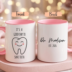 May include: White ceramic mug with a pink interior and handle. The front of the mug features a smiling tooth graphic and the text "IT'S A GOOD DAY TO SAVE TEETH." The back of the mug has the text "Dr. Madison EST. 2026."