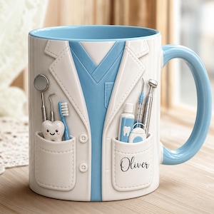 May include: A white ceramic mug featuring a 3D-style design of a white lab coat over a light blue scrub top. The mug displays dental tools, a toothbrush, a tube of toothpaste, and a smiling tooth character. The name Oliver is printed on the pocket.