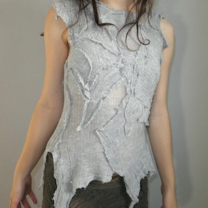 May include: A light gray, sleeveless top with a distressed, textured design. The fabric appears to be loosely woven, with jagged edges and an irregular pattern. The top has a unique, artistic aesthetic.