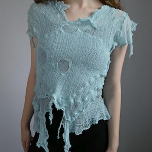 May include: A light blue short-sleeved top made of a sheer, open-knit fabric with a distressed, frayed texture. The garment features a wide, uneven neckline and jagged, asymmetrical hemline with loose hanging threads throughout the design.