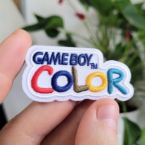 May include: White embroidered patch with the text "GAME BOY COLOR" in blue, red, yellow, and green lettering.
