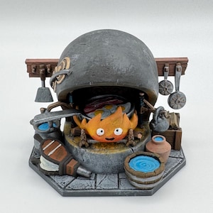 May include: A detailed, miniature sculpture of a kitchen scene. A fiery character is inside a large, gray oven. The scene includes miniature pots, pans, and water barrels. The base is a gray, stone-like material.