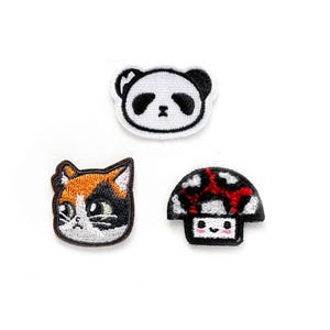 Può includere: Tre toppe ricamate da stirare che raffigurano un panda bianco e nero, un gatto calico e un fungo rosso e bianco.