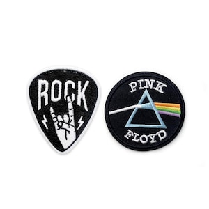 Op de afbeelding: Twee zwarte en witte geborduurde strijkpatches. Eén patch is gevormd als een gitaarplectrum en zegt "ROCK" met een witte hand die het rock-and-roll-teken maakt. De andere patch is rond en zegt "PINK FLOYD" met een witte driehoek en een regenbooglichtstraal.