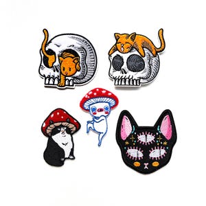 Può includere: Cinque toppe ricamate da stirare che raffigurano un gatto nero con tre occhi, un fungo con una creatura bianca al suo interno, uno scheletro con un gatto in cima, uno scheletro con un gatto all'interno e un gatto con uno scheletro sulla testa.