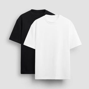 Pode incluir: Duas camisetas, uma preta e uma branca, são colocadas em um fundo cinza. Ambas as camisetas têm mangas curtas e gola redonda.