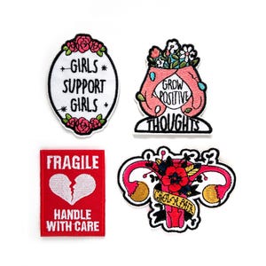 Puede incluir: Cuatro parches bordados para planchar con temas feministas. El primer parche es rosa y blanco con el texto "Girls Support Girls". El segundo parche es rosa y blanco con el texto "Grow Positive Thoughts". El tercer parche es rojo con el texto "Fragile Handle With Care" y un corazón roto. El cuarto parche es rosa y blanco con un útero estilizado con flores y el texto "Grow a Pair".